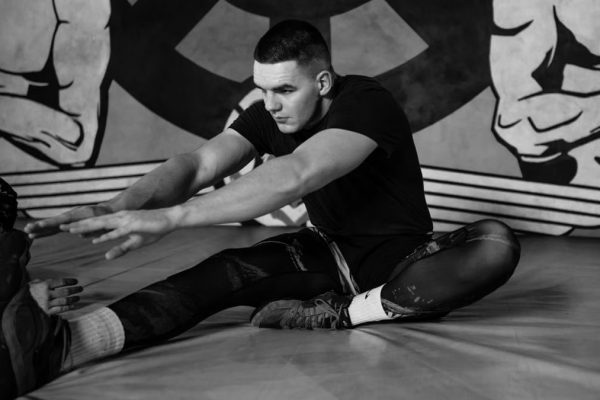 Focused adult male athlete stretching on a gym mat amidst training, capturing strength and concentration.
