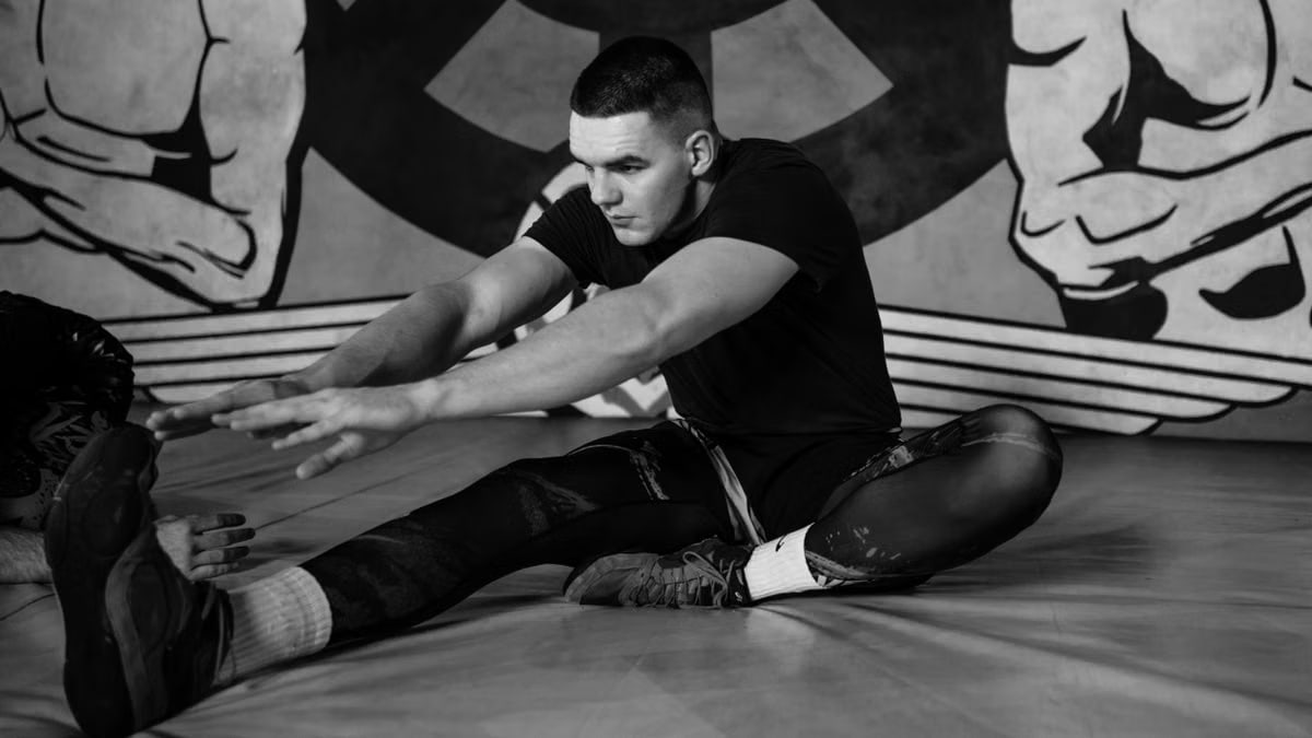 Focused adult male athlete stretching on a gym mat amidst training, capturing strength and concentration.